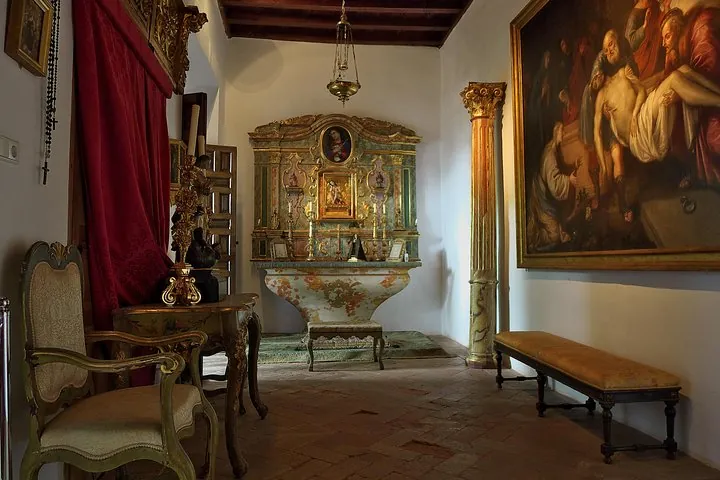 A small chapel with a gilded altarpiece, a large religious painting and a carved bench