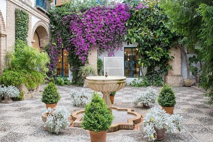 A stone fountain among clipped shrubs and a wall of purple bougainvillea